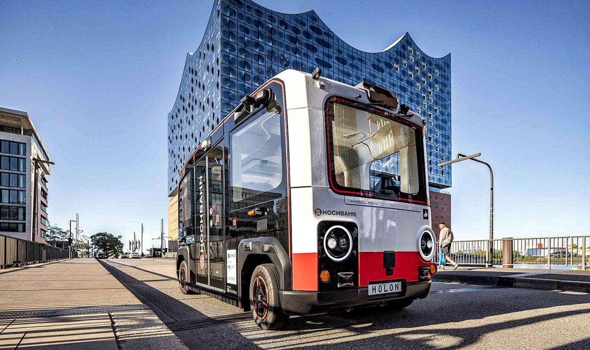 Ein autonom fahrender Shuttle-Bus des Typs HOLON mit HOCHBAHN-Branding fährt vor der Hamburger Elbphilharmonie. Das Bild illustriert die abgeschlossene Fahrzeugpotenzialstudie des Projekts FAST Hamburg zur Nutzung autonomer Fahrzeuge im öffentlichen Nahverkehr.