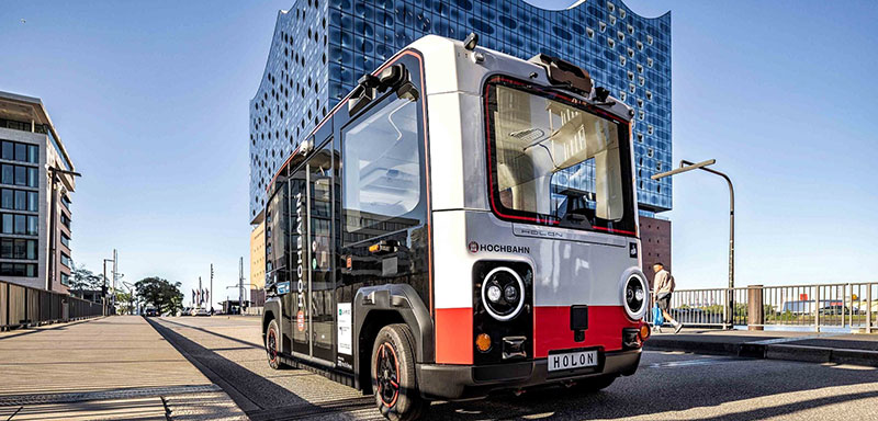 Ein autonom fahrender Shuttle-Bus des Typs HOLON mit HOCHBAHN-Branding fährt vor der Hamburger Elbphilharmonie. Das Bild illustriert die abgeschlossene Fahrzeugpotenzialstudie des Projekts FAST Hamburg zur Nutzung autonomer Fahrzeuge im öffentlichen Nahverkehr.