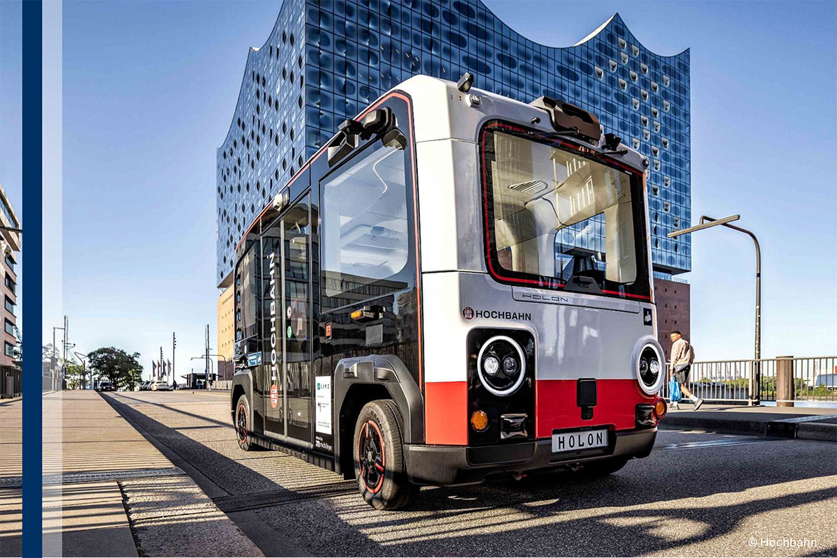 in autonom fahrender Shuttle-Bus des Typs HOLON mit HOCHBAHN-Branding fährt vor der Hamburger Elbphilharmonie.